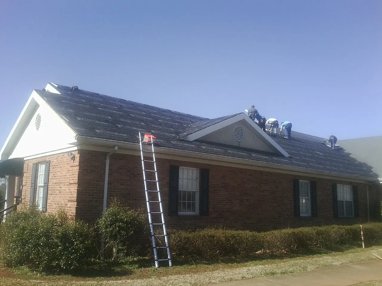 Crew tearing shingles off a brick ranch roof with a ladder set — Emergency Roof Repair work by our crew in Allston