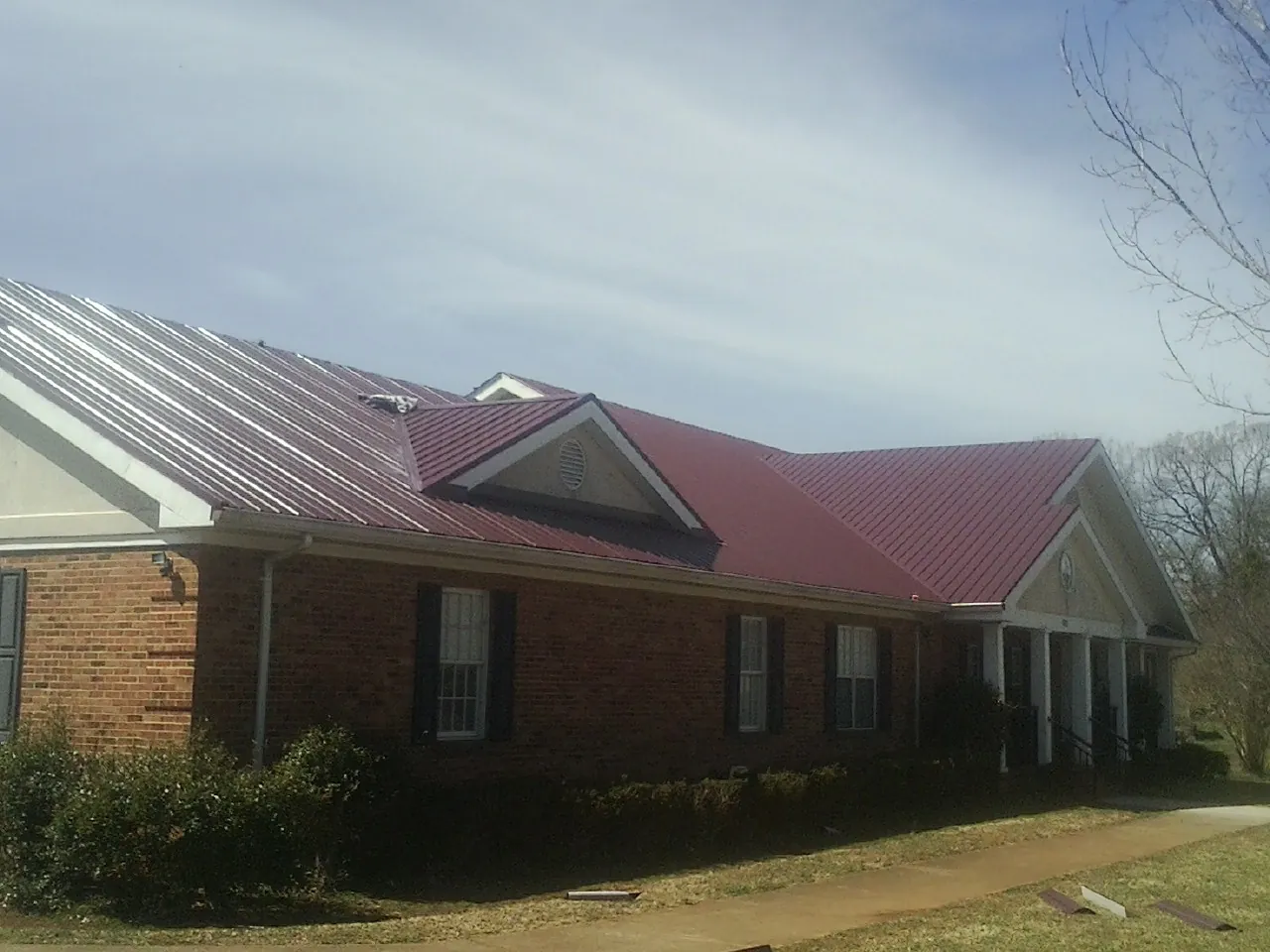 Red metal roof with gabled entries on a long brick building, from a Hail Damage Roof Repair job in Allston