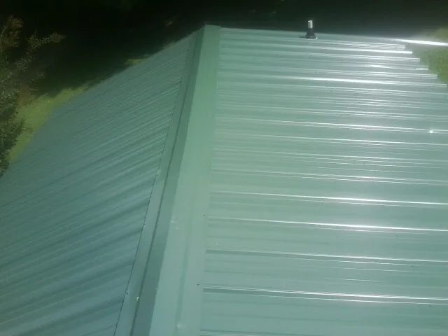 New green metal panels meeting at the ridge of a roof — Flat Roof Repair work by our crew in Allston