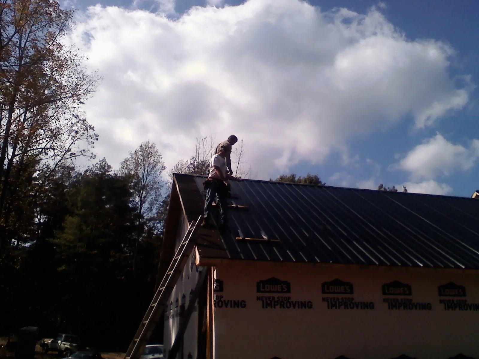 Roofer fastening dark metal panels high against a cloudy sky, from a Roof Inspection job in Allston