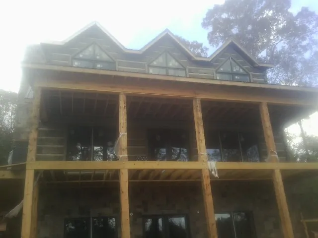Dormers and porch framing on a large log home under construction — Roof Coating work by our crew in Allston
