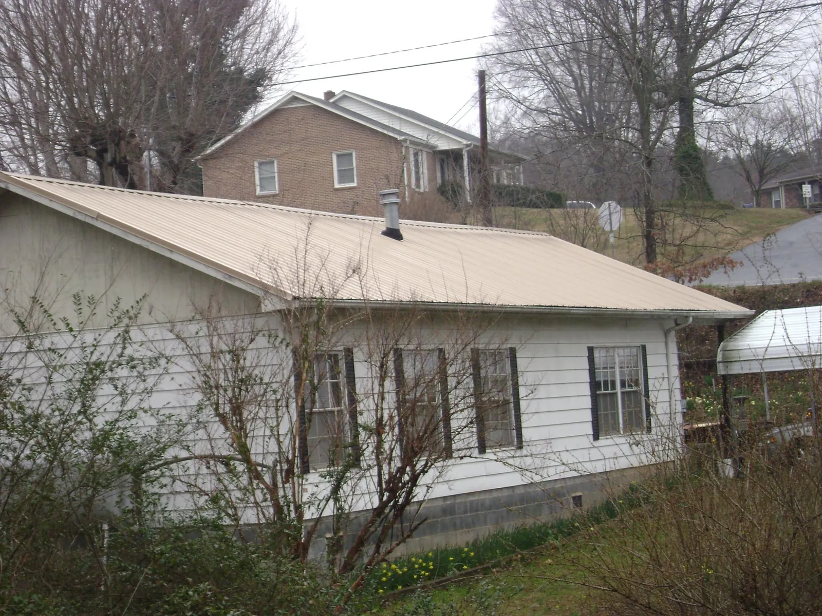 Tan metal roof on a white sided house set into a hillside — Commercial Roofing by Roofing Brothers in Allston