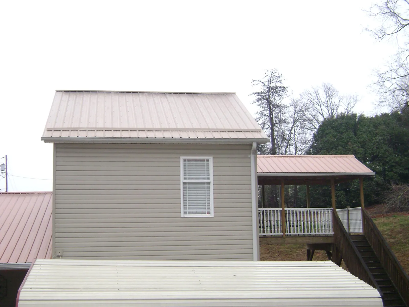 Tan metal roofs on a two story addition and attached porch, from a Roof Replacement job in Allston